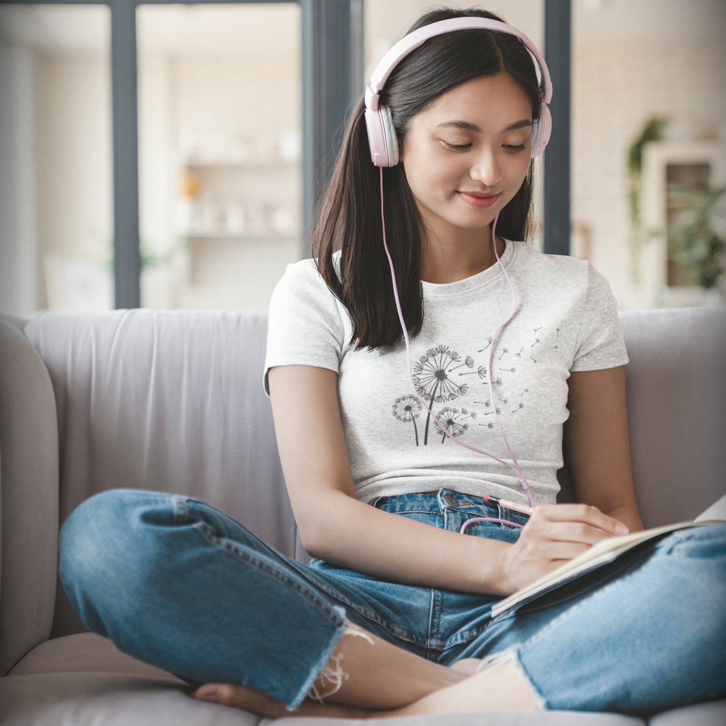 Woman sitting on a couch wearing headphones and writing in journal.