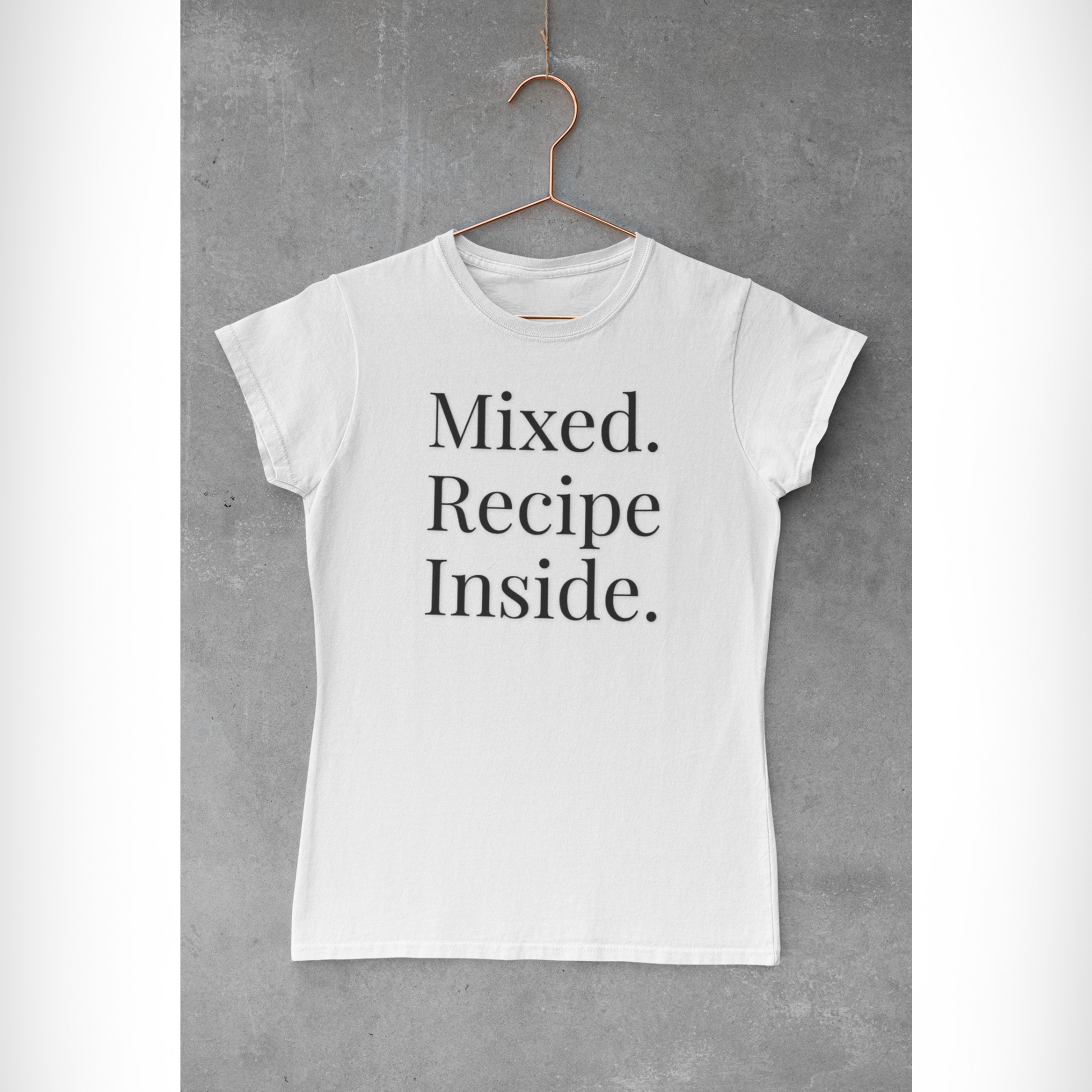 Unisex White Origin — Signature Tee with “Mixed. Recipe Inside.” text across chest, hanging on a rose gold hanger against a cement background - stacked wordmark; front view, minimal-luxe, soft cotton texture.