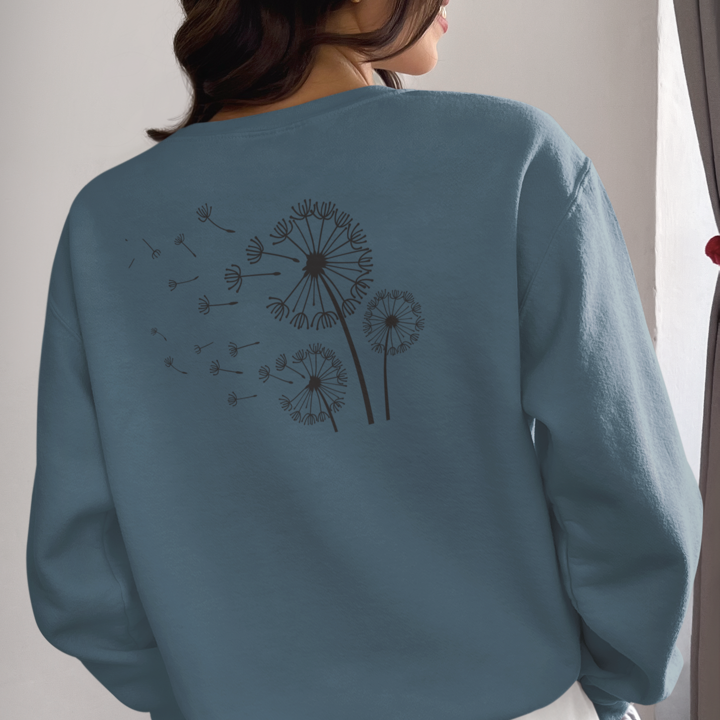 Blue sweatshirt with dandelion design on the back, worn by a person.