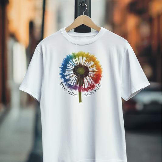 White t-shirt with a colorful dandelion graphic and Every Color. Every Seed. text centered front, on a hanger against a blurred background