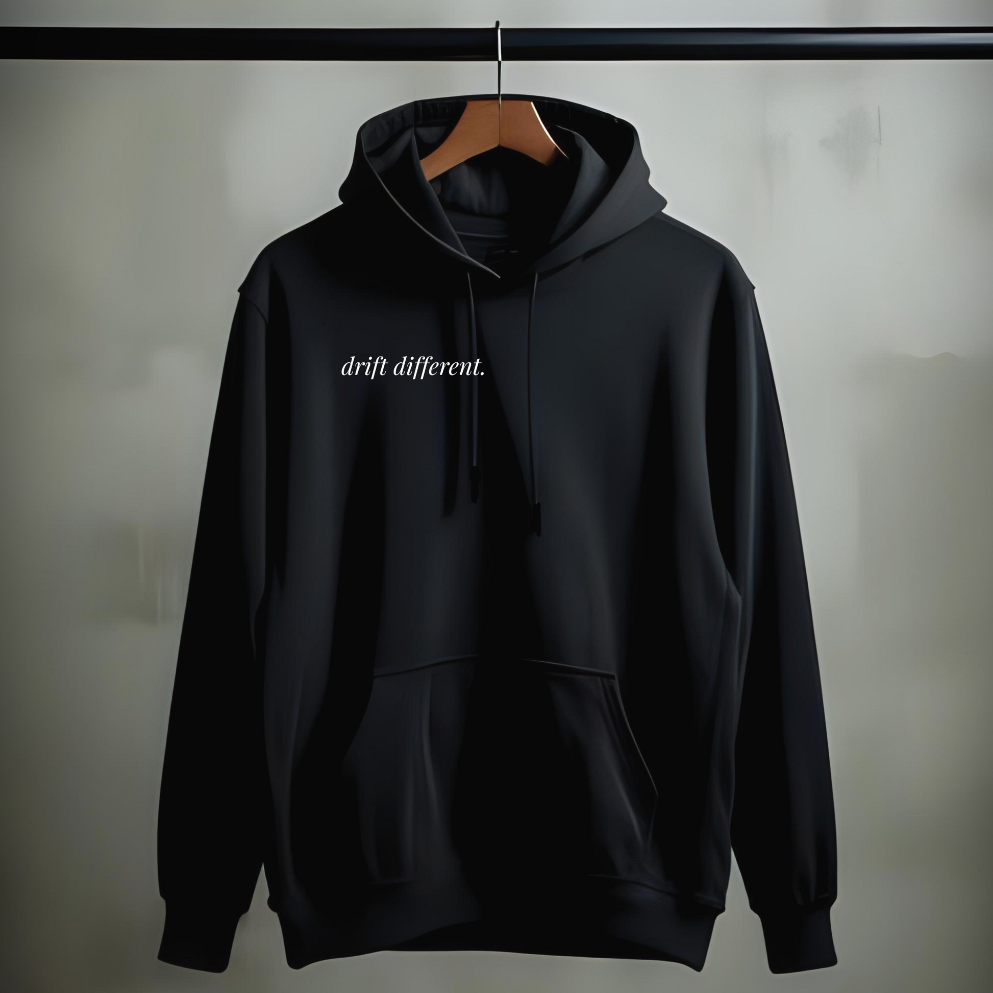 Black drift different. hoodie with minimalist chest print on a wooden hanger against a neutral background