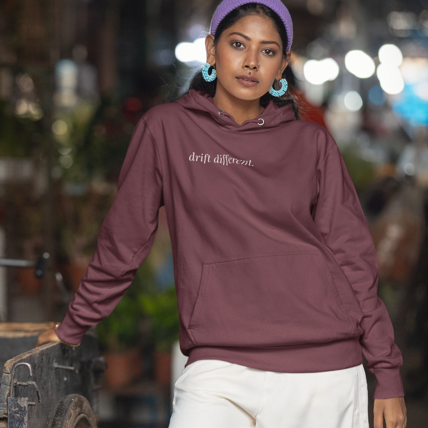 Woman wearing a maroon hoodie with 'drift different' text, standing outdoors with a blurred background.