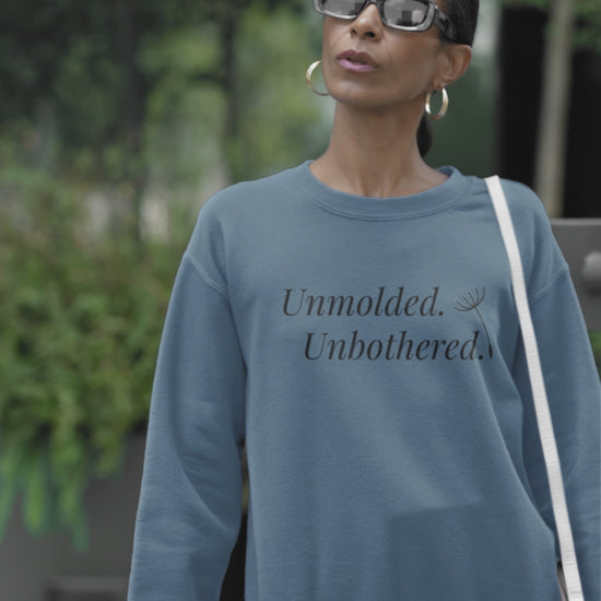 Video of a woman wearing an indigo blue Unmolded. Unbothered. sweatshirt, standing in a park.